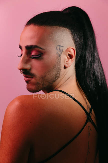Vista laterale ritratto di glamour transgender donna barbuta in sofisticato make up in posa con gli occhi chiusi contro sfondo rosa in studio — Foto stock
