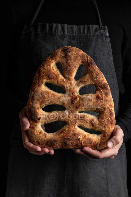 Crop chef masculino en delantal de pie con pan recién horneado de fougasse pan - foto de stock