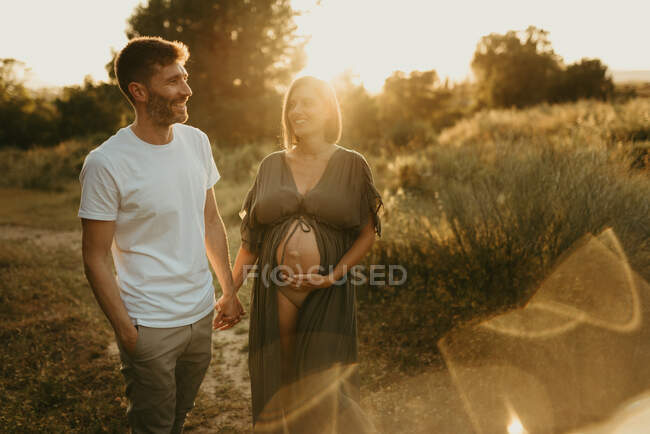 Розчарований чоловік тримає за руку вагітну жінку, стоячи разом під час заходу сонця. — стокове фото