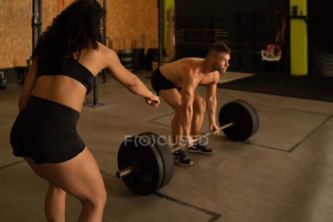 Apto atleta masculino fazendo exercício deadlift com barra sob supervisão de treinador pessoal feminino durante o treino no ginásio — Fotografia de Stock