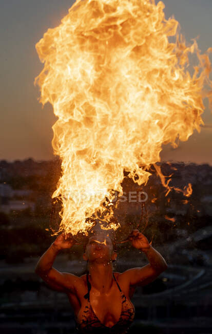 Mujer devoradora de fuego realizando fuego de saliva al atardecer - foto de stock