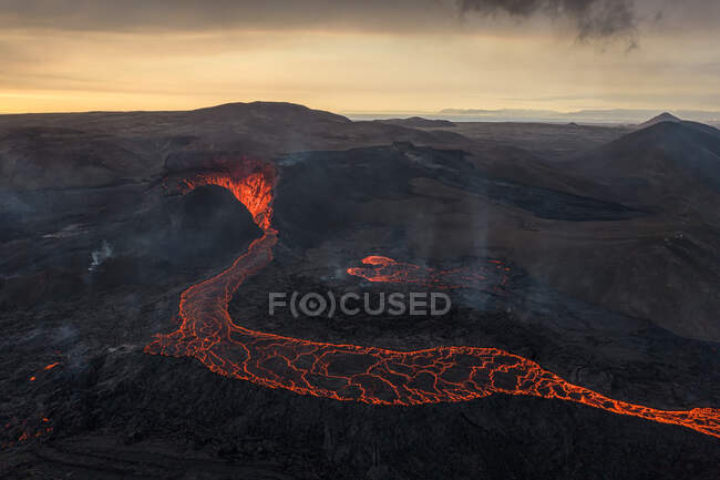 Drohnenblick auf den Strom heißer orangefarbener Lava, der am Morgen durch bergiges Gelände in Island fließt — Stockfoto