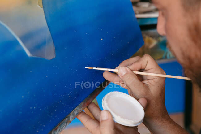 Cropped unrecognizable bearded man painting dots with white pigment on canvas with abstract picture during work in creative workshop — Stock Photo