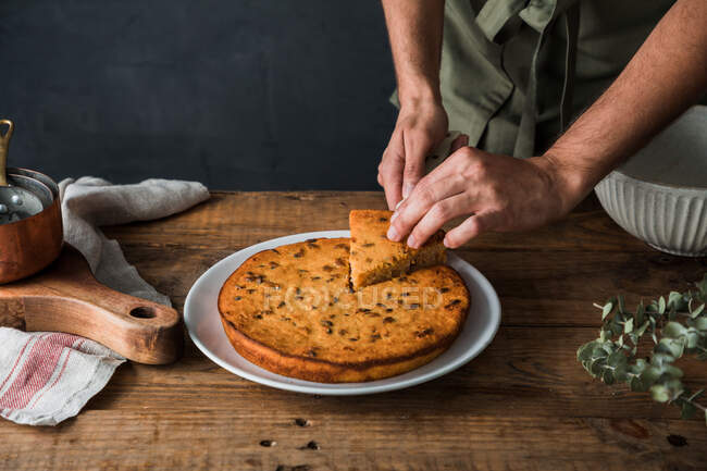 Высокий угол анонимного мужчины-повара, берущего кусок вкусного тыквенного пирога с тарелки на деревянном столе — стоковое фото