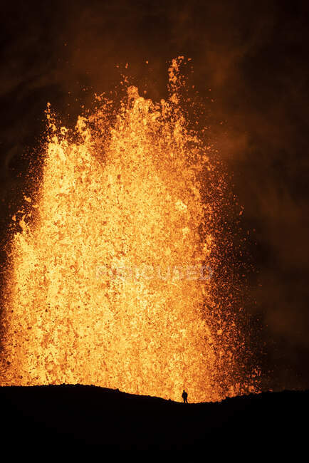 Silueta de viajero anónimo de pie contra el humo naranja del volcán activo en Islandia - foto de stock