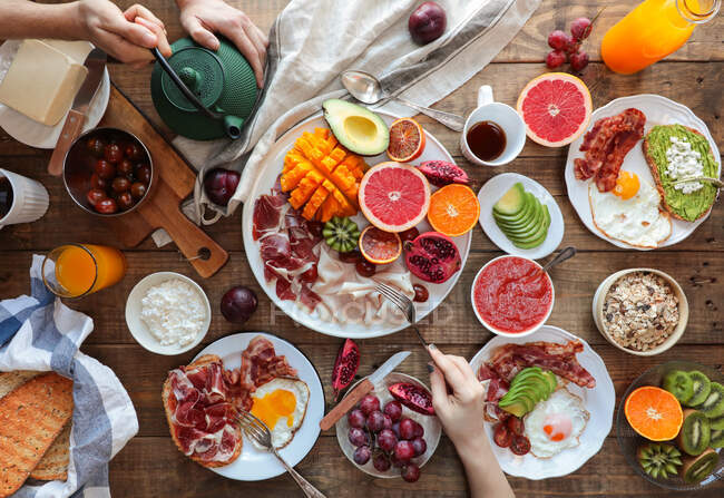 Dall'alto ampia vista del tavolo in legno con molteplici pasti sani preparati per la colazione. Coltivare le mani con utensili da cucina — Foto stock