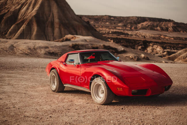 Luxury red sports car parked near mountain peak against cloudy sky in desert of Bardenas Reales Natural Park in Navarra, Spain — Stock Photo