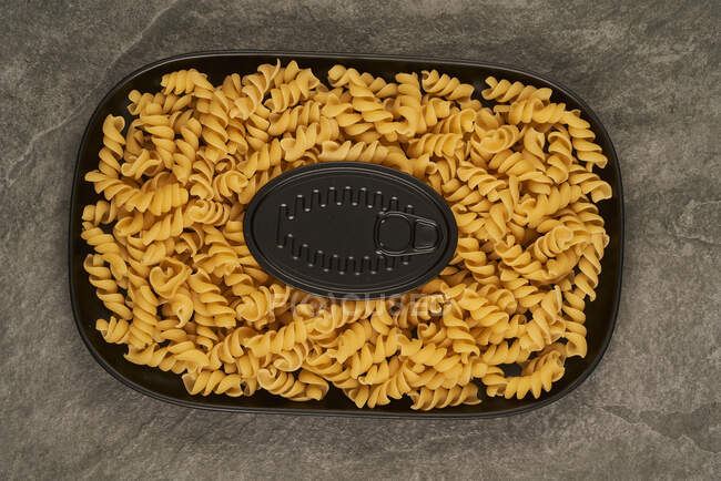 Ansicht der schwarzen Dose in der Nähe von ungekochten Fusilli-Nudeln auf Tablett auf dem Tisch — Stockfoto