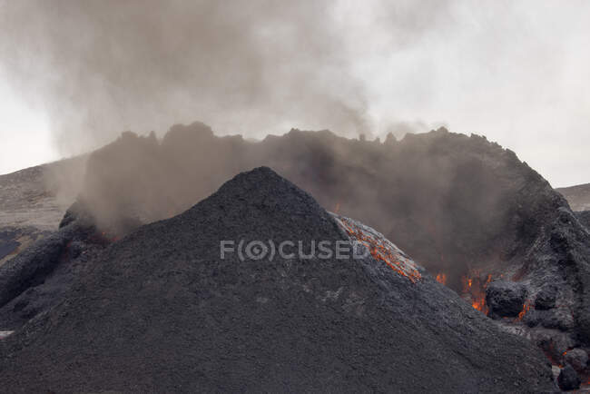 Cráter áspero del volcán activo que emite humo espeso en día gris en Islandia - foto de stock