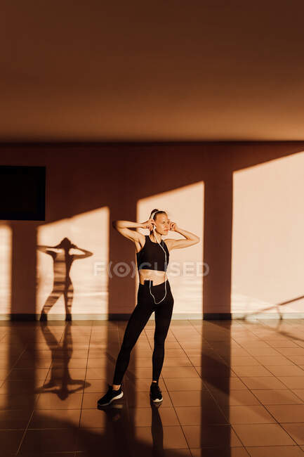Giovane donna atletica caucasica che ascolta musica ad occhi chiusi e si rilassa al tramonto, ombre e luce sullo sfondo — Foto stock