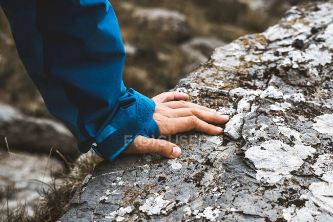 Dall'alto mano della persona viaggiatore raccolto in giacca blu brillante appoggiata sulla collina rocciosa — Foto stock