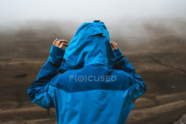 Back view of unrecognizable tranquil woman in bright blue jacket standing on rocky hill — Stock Photo