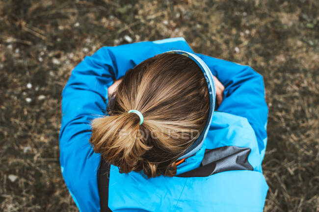 Top view of unrecognizable tranquil woman in bright blue jacket having rest sitting with backpack enjoying views looking away in dry valley in foggy haze — Stock Photo
