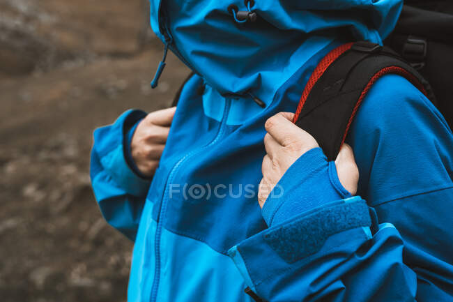 Crop woman traveling in comfortable blue jacket and fastening backpack button — Stock Photo