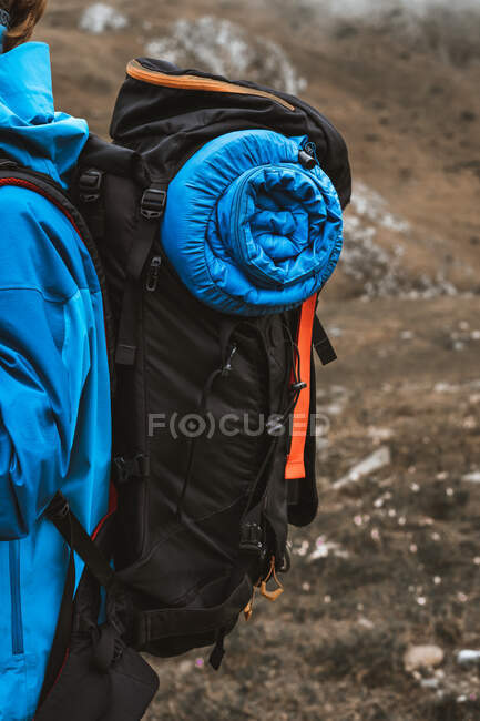Vista lateral da mulher anônima tranquila em casaco azul brilhante com mochila em pé na colina rochosa — Fotografia de Stock