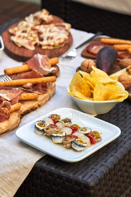 Haut angle de délicieux légumes marinés brochés avec des sardines, des olives poivron rouge et oignon bébé placé sur la table avec un assortiment de collations — Photo de stock