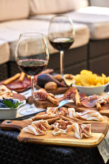 Köstlicher Speck serviert auf einem Holzbrett auf dem Tisch mit verschiedenen Vorspeisen und Gläsern Rotwein — Stockfoto