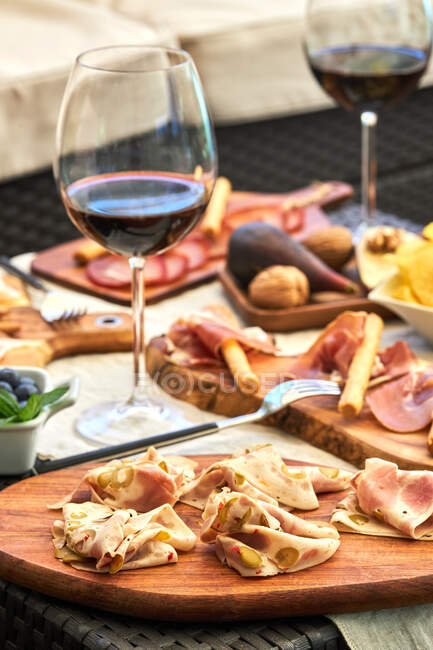 Delicious bacon served on wooden cutting board on table with various appetizers and glasses of red wine — Stock Photo