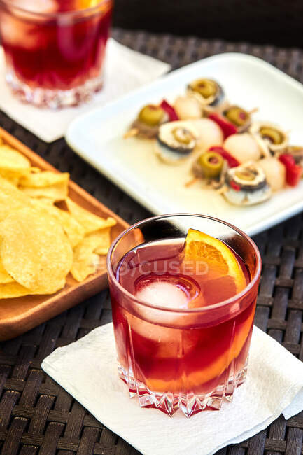 From above of glass with cold old fashioned cocktail with ice and orange slice served on table with appetizers — Stock Photo