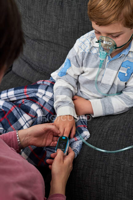Cortar mulher irreconhecível usando oxímetro de pulso moderno no dedo da criança para medir o nível de oxigênio no sangue — Fotografia de Stock