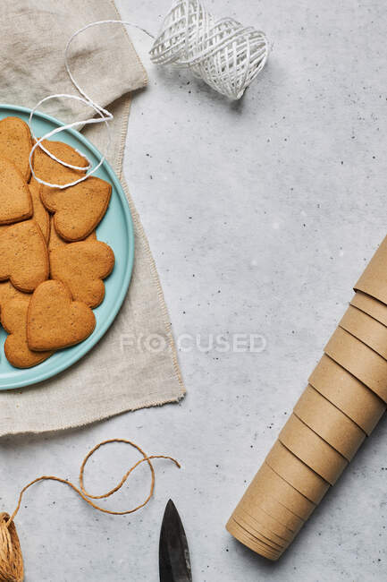 Vista superior do layout de biscoitos de Natal em forma de coração doce na placa e materiais de embalagem variados na mesa — Fotografia de Stock