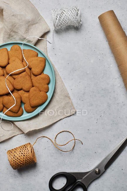 Vista superior del diseño de galletas de Navidad en forma de corazón dulce en el plato y materiales de embalaje surtidos en la mesa - foto de stock