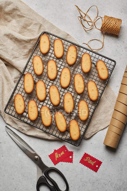 From above of tasty Christmas biscuits placed on metal baking net on table with assorted wrapping supplies — Stock Photo