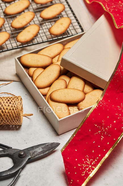 From above of tasty Christmas biscuits placed on metal baking net and box on table with assorted wrapping supplies — Stock Photo