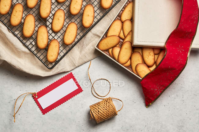 Dall'alto di gustosi biscotti natalizi posti su rete da forno in metallo e scatola sul tavolo con forniture di imballaggio assortite — Foto stock