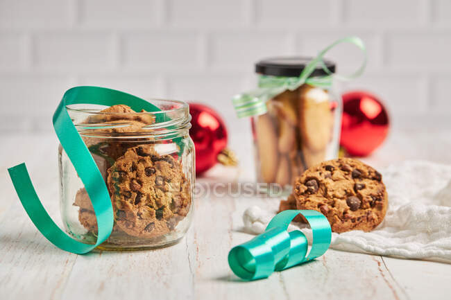 Homemade chocolate chip Christmas biscuits in glass jars placed on table with ribbons and baubles — Stock Photo