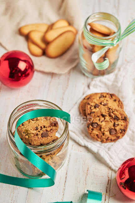 From above homemade chocolate chip Christmas biscuits in glass jars placed on table with ribbons and baubles — Stock Photo