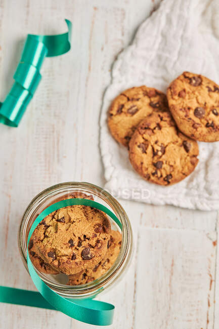 From above homemade chocolate chip Christmas biscuits in glass jars placed on table with ribbons and baubles — Stock Photo