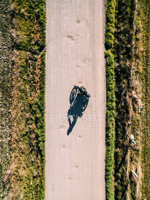 De cima vista aérea da pessoa dirigindo moto na estrada rural à luz do sol no campo — Fotografia de Stock