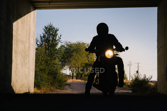 Silhueta de piloto irreconhecível sentado em moto com faróis ligados em túnel — Fotografia de Stock