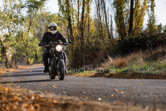 Man in leather jacket and helmet riding bike on asphalt road in sunny autumn day in countryside — Stock Photo