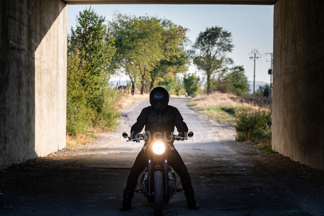 Silhouette de coureur méconnaissable assis sur la moto avec allumé les phares dans le tunnel — Photo de stock