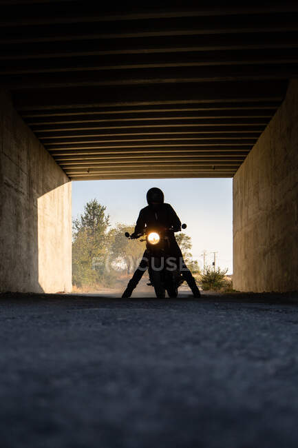 Silueta de corredor irreconocible sentado en moto con faros encendidos en túnel - foto de stock