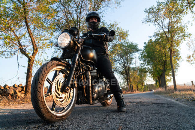 Homem de jaqueta de couro e capacete andar de bicicleta na estrada de asfalto no dia ensolarado de outono no campo — Fotografia de Stock