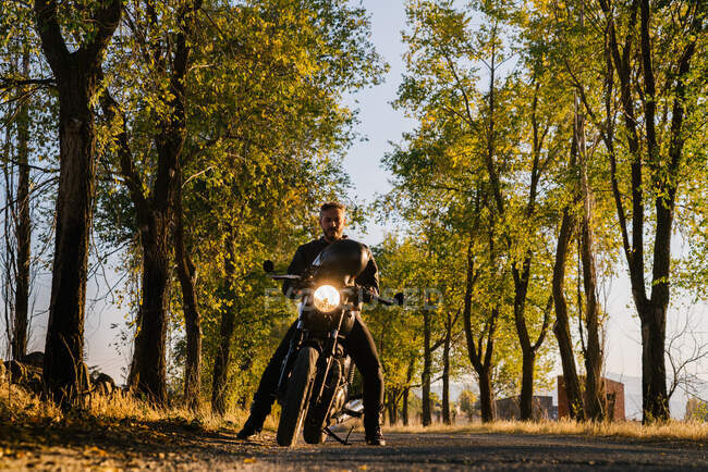 Man in leather jacket riding bike on asphalt road in sunny autumn day in countryside — Stock Photo