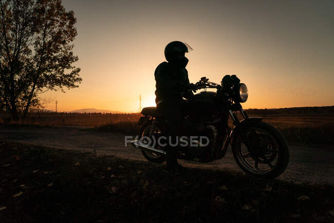 Gesichtsloser Biker mit Helm fährt Motorrad bei Sonnenuntergang auf Landstraße — Stockfoto