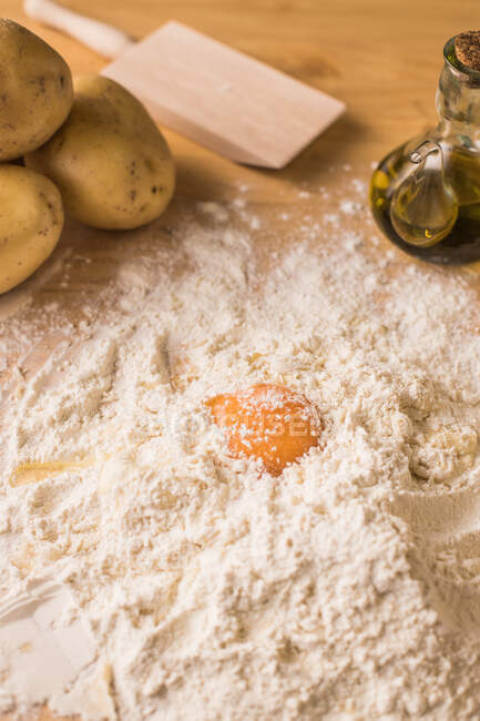 From above egg yolk placed on heap of wheat flour near potatoes and oil during gnocchi dough preparation on table in kitchen — Stock Photo