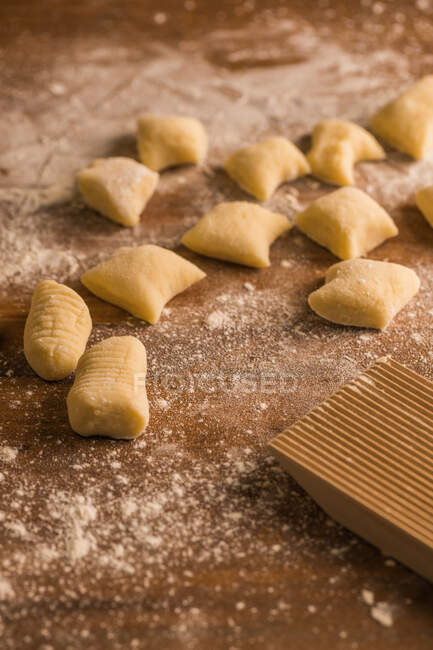 Top view of pieces of soft raw tough placed on wooden table covered with flour near ribber board during gnocchi preparation in the kitchen — стоковое фото