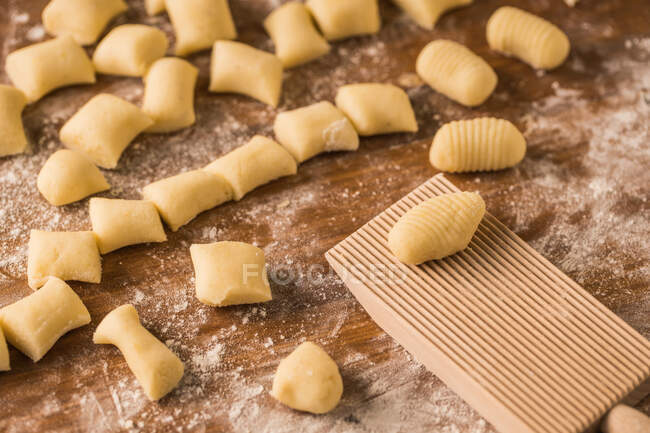 Draufsicht auf weiche rohe Teigstücke, die während der Gnocchi-Zubereitung in der Küche auf einem Holztisch mit Mehl bedeckt sind — Stockfoto