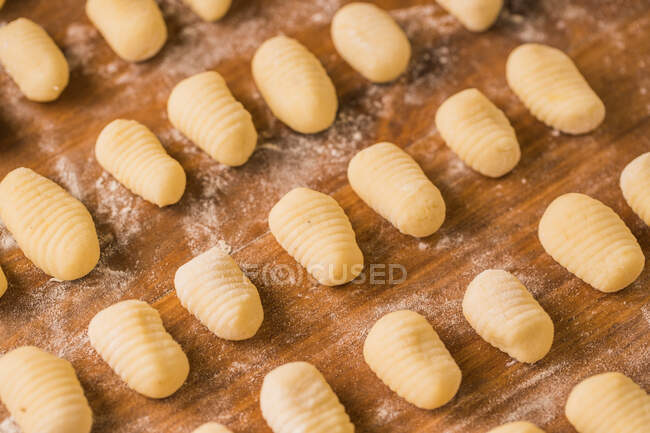 Vue du dessus des gnocchis non cuits placés en rangées organisées sur la table de bois pendant la préparation du déjeuner à la maison — Photo de stock