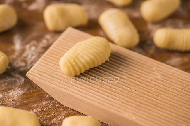 Top view of pieces of soft raw tough placed on wooden table covered with flour near ribber board during gnocchi preparation in the kitchen — стоковое фото