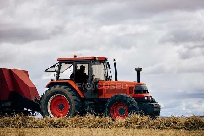 Сушеный сеновальный рулон и современный трактор размещены на сельскохозяйственном поле в горной местности летом — стоковое фото