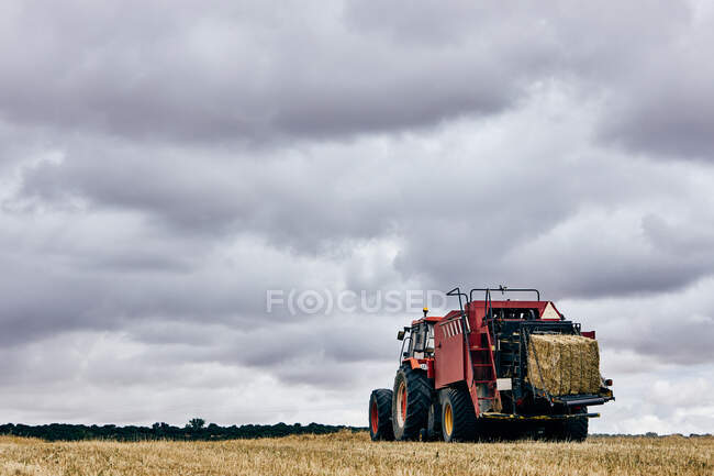 Dried hay roll and modern tractor placed on agricultural field in mountainous area in summer — Stock Photo