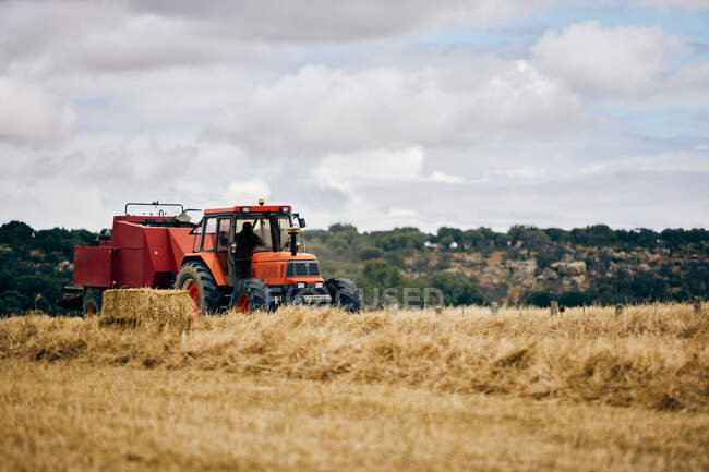 Сушеный сеновальный рулон и современный трактор размещены на сельскохозяйственном поле в горной местности летом — стоковое фото