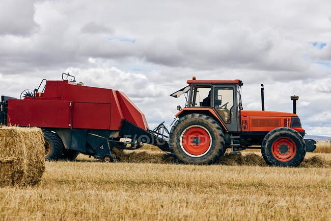 Rouleau de foin séché et tracteur moderne placé sur un champ agricole en zone montagneuse en été — Photo de stock