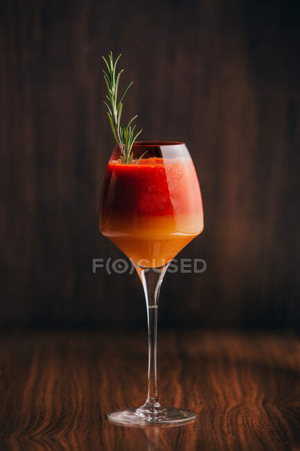 Vue rapprochée du cocktail rouge et orange au romarin placé sur une surface en bois — Photo de stock
